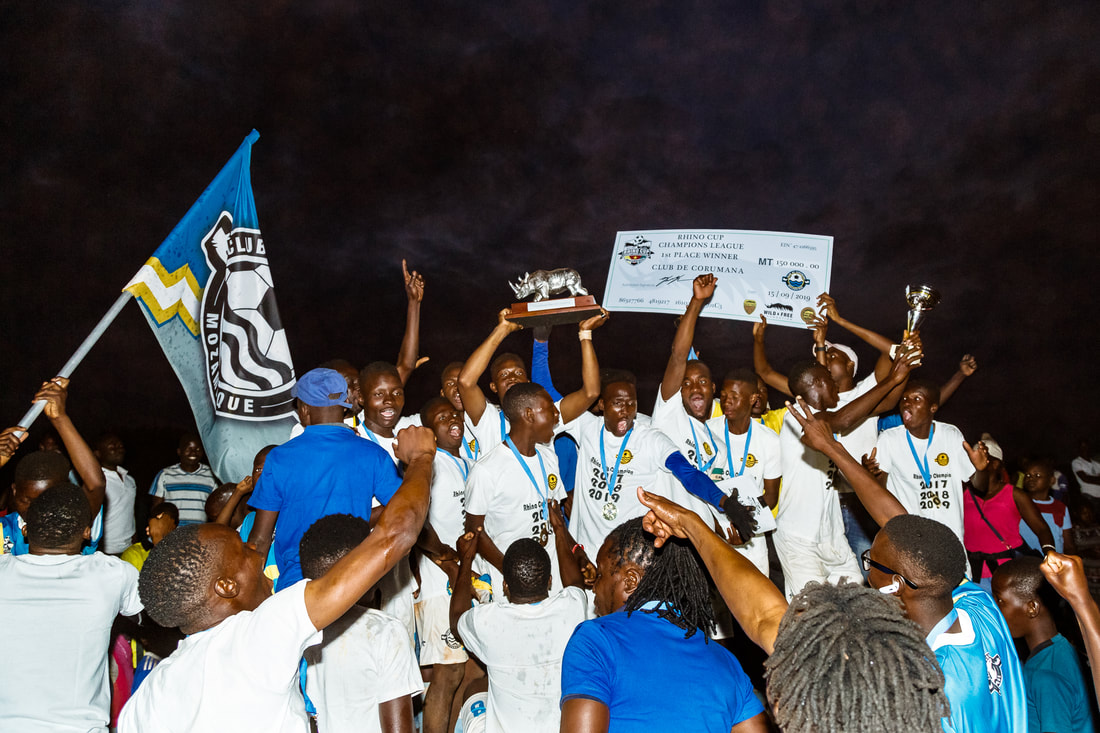 Bito Billa, with an exciting display of emotion, poses for a photo with fellow team members after Corumana FC won the Rhino Cup Champions League for the third time in a row. Bito, with his team players, is holding up the Rhino Cup trophy and the winning cheque of 150,000.00 Mozambican Meticals. This special moment took place during the closing award ceremony on the Corumana soccer pitch in Mozambique.
