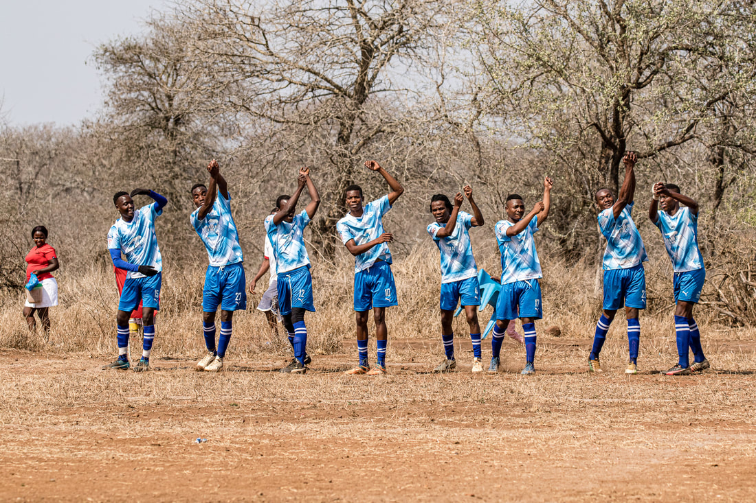 In this image, Bito Billa and seven fellow team players are celebrating a goal. They all imitate a victory 