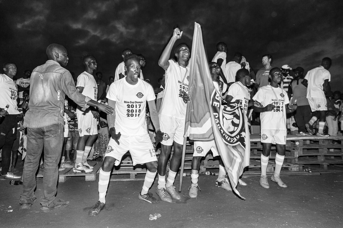 Bito Billa, with an exciting display of emotion, poses for a photo with fellow team members after Corumana FC won the Rhino Cup Champions League for the third time in a row. This special moment, in a black and white photo, took place during the closing award ceremony on the Corumana soccer pitch in Mozambique.
