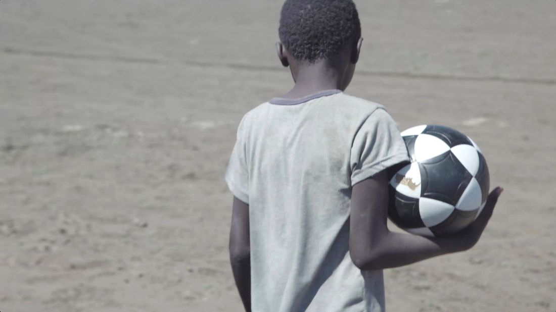 A young man holds a soccer ball with the Rhino Revolution logo on it. This moment was captured near the Pafuri border gate that separates the Kruger National Park between Mozambique and South Africa. An image from the Rhino Cup Champions League season in 2018.
