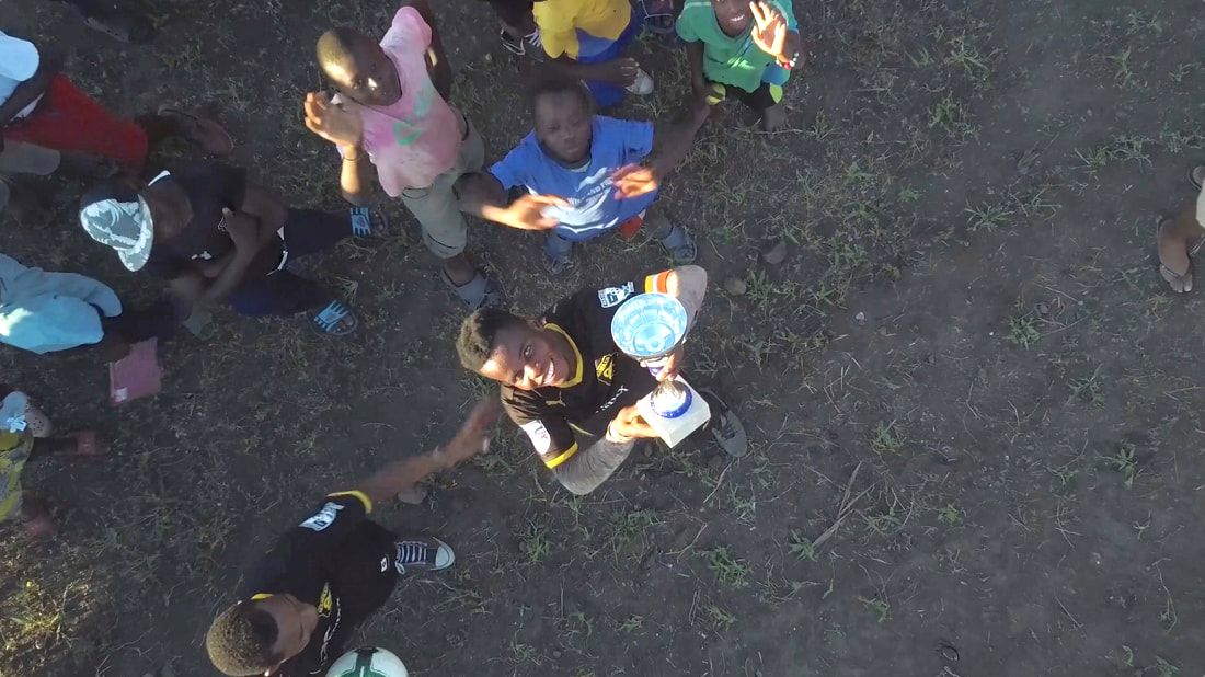 This photo is an aerial shot of a soccer player holding up a trophy that his team won during a tournament that was held near the Pafuri border gate that separates the Kruger National Park between Mozambique and South Africa.