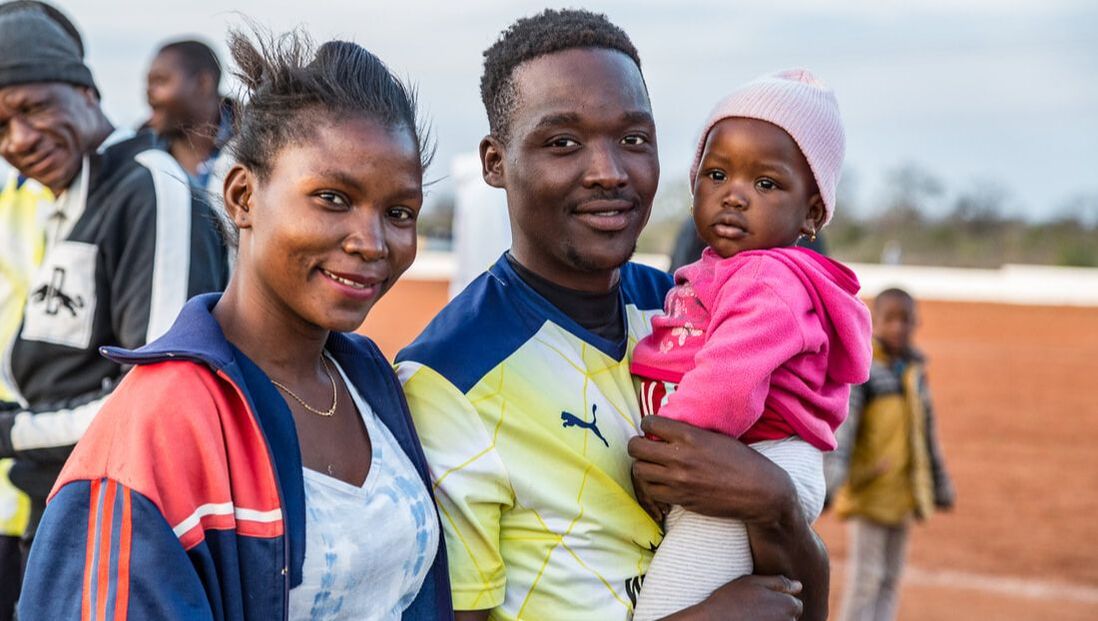 In this image, Bito Billa is standing next to his wife. He is holding his baby daughter (two years old) in his arms, and his wife has an expression of pride and joy. Corumana FC in their yellow kit for the 2019 Rhino Cup Champions League season won against Chelsea FC on the Corumana soccer field, Mozambique. The Corumana FC team is sponsored by Wild and Free Foundation.