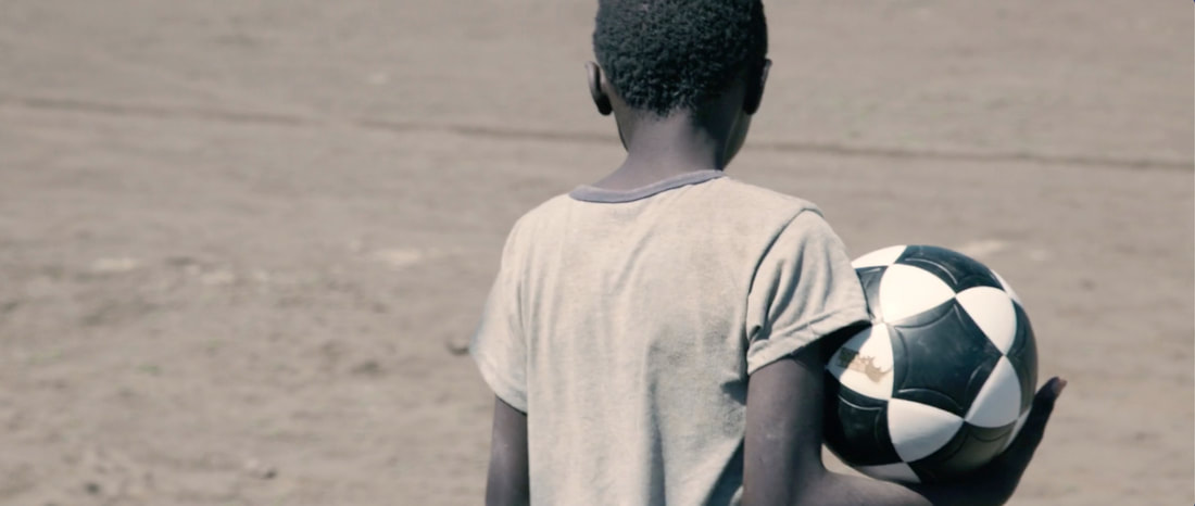 Image of a young child holding a sponsored soccer ball, with a Rhino Revolution logo printed on the ball. Preview image from the Rhino Cup Documentary, produced by Myles Pizzey.