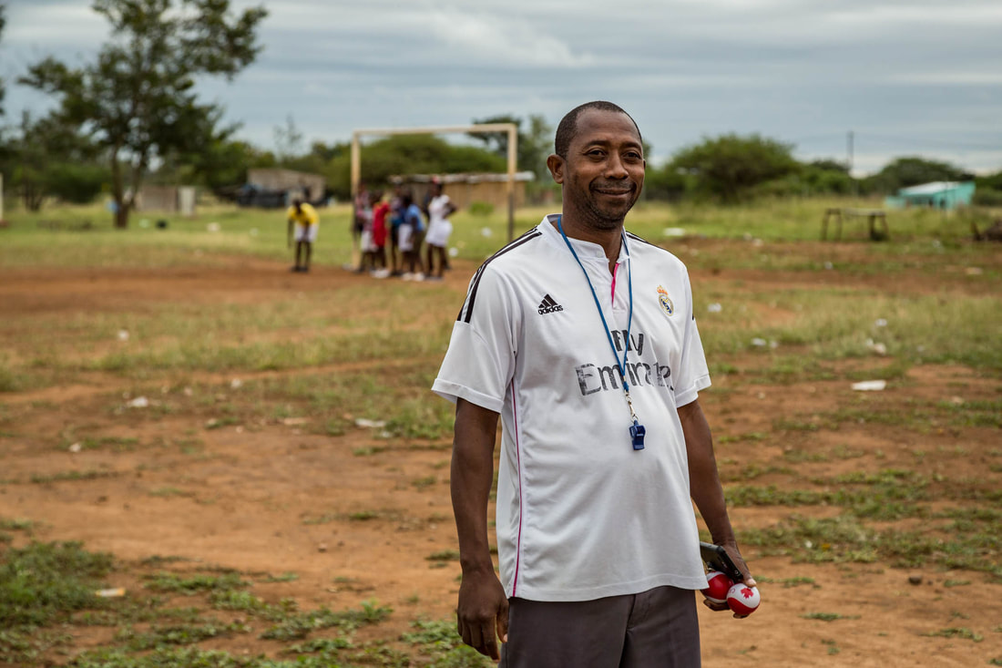 Mr. Rodrigues Bitone, posed for this photo during a coaching session for the female soccer team Peregrinas de Sabie F.C. (in the background). Mr. Bitone is the Chairman of the women's league committee.
