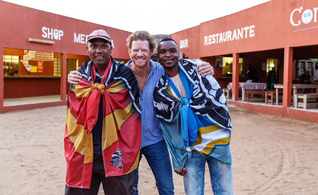 In this photo is Bernardo Malavela (left), Matt Bracken (middle) and Orlando “Watch” Cossa (right). Two committee members of the Rhino Cup Champions League, joined by the co-founder of Wild and Free Foundation, for a photo in front of their favorite restaurant in Sàbié, Mozambique. Photo taken in the afternoon at a meeting during the 2019 RCCL season. Image taken at a local restaurant known as “Banana Landia” or Tshakane restaurant.