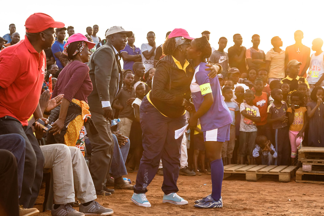 Mrs. Helena Alfredo Chivite (Head of the Administrative Post of Sábiè) congratulates Hanifa Vasco Manjate, Captain of the Peregrinas de Sabie F.C., after Hanifa delivered her message to the athletes for the 2019 Rhino Cup Champions League prize-giving ceremony, at the Corumana soccer field, Mozambique.