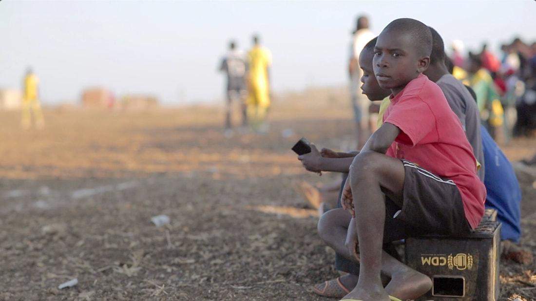 An image of a young soccer fan sitting on an old beer crate and supporting the Club de Corumana and Freitas FC teams, sitting next to the dusty gravel pitch of Corumana soccer field, August 27, 2016. Wild and Free Foundation's goal is to create a community driven conservation initiative.